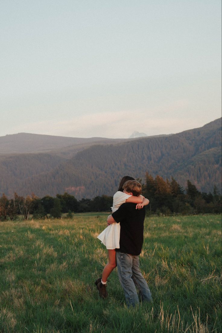 a man and woman hug in the middle of a field with mountains in the background