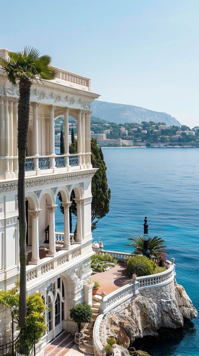 a large white building sitting on the side of a body of water next to a lush green hillside