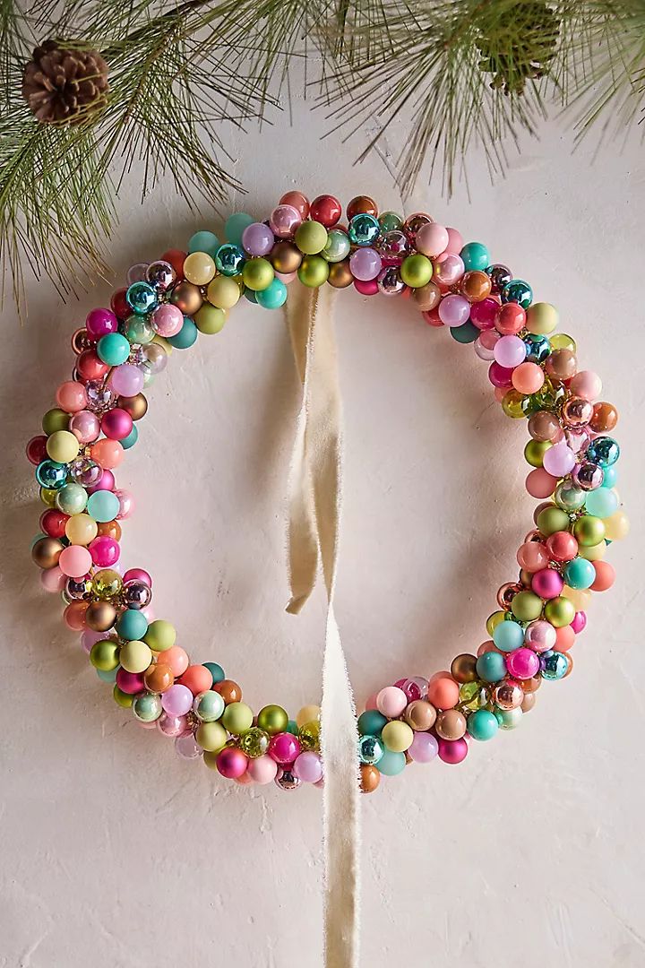 an ornament made out of beads on a white surface next to a pine tree