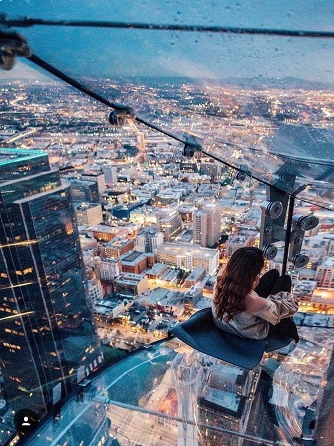 a woman sitting on top of a tall building looking down at the city from above