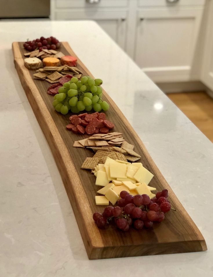 a wooden platter filled with grapes, cheese and crackers on top of a kitchen counter