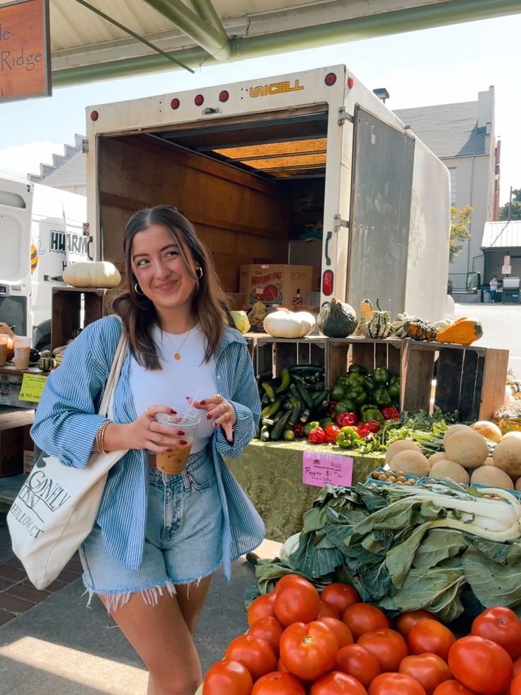 a woman standing next to a pile of tomatoes