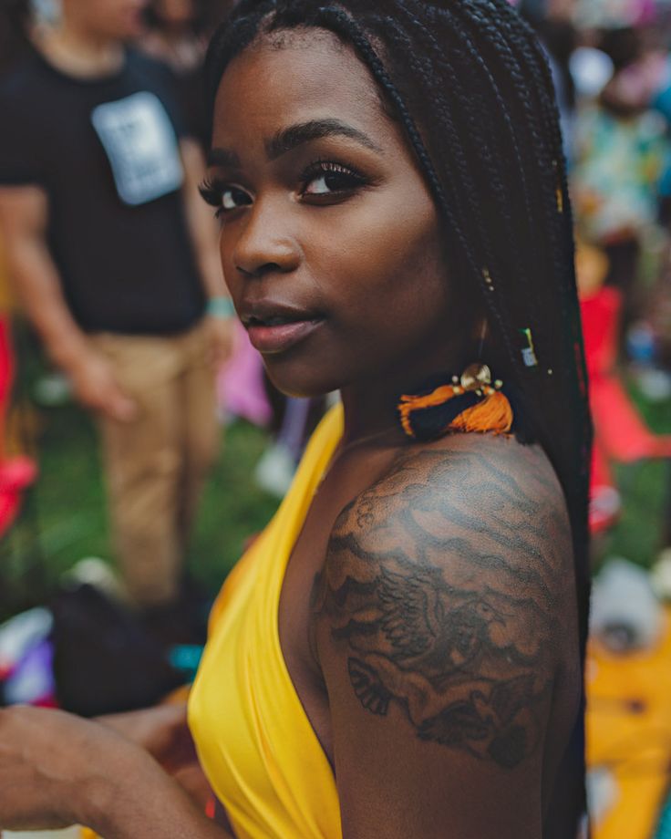 a woman with tattoos on her arm and chest standing in front of other people at an outdoor event