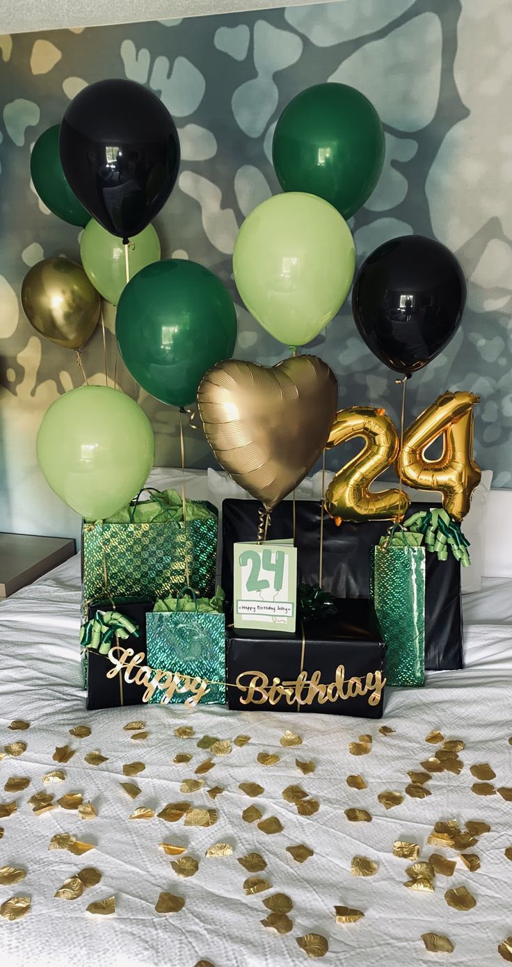 a bed topped with lots of green and gold balloons next to a black box filled with presents