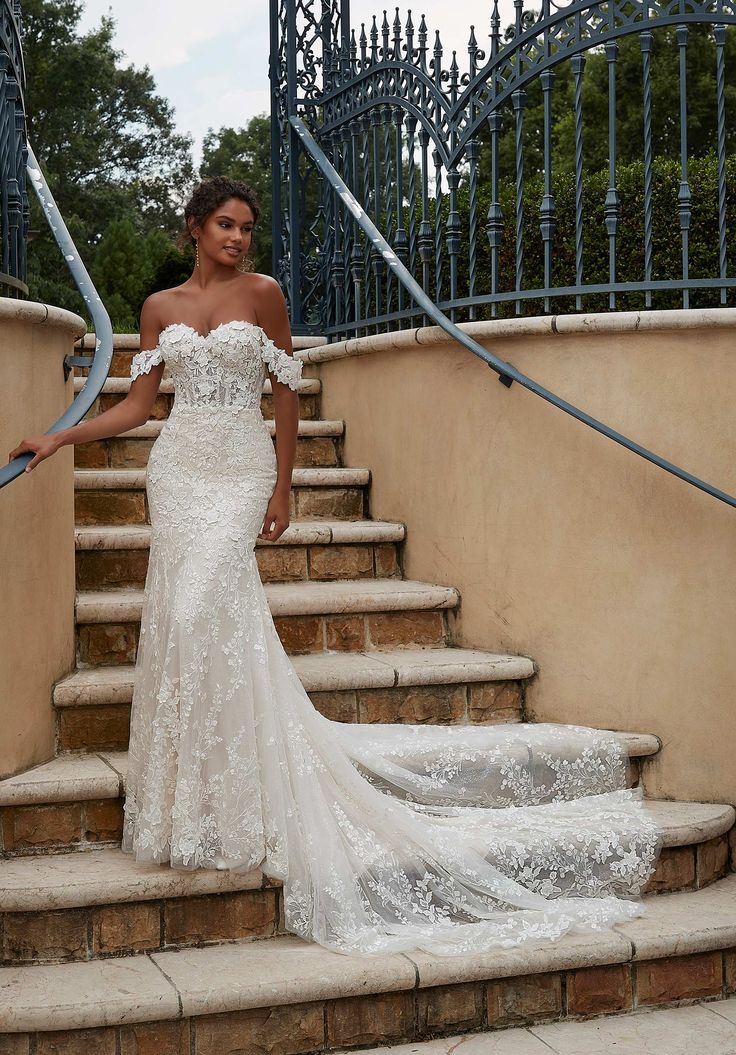 a woman in a white wedding dress standing on some steps with her arms around her waist