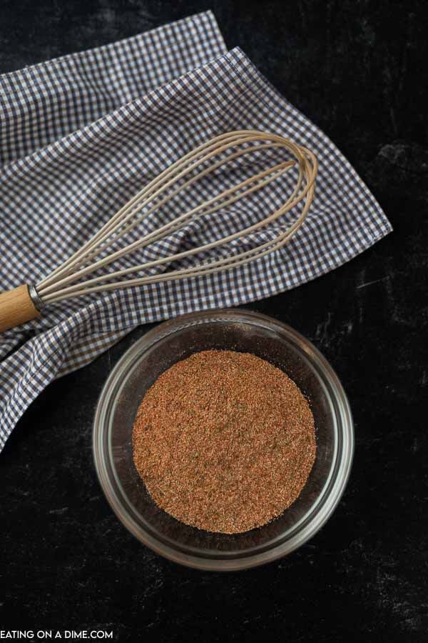 a glass bowl filled with spices next to a whisk on top of a checkered cloth