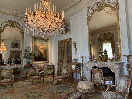 an ornately decorated living room with chandelier and paintings on the walls, along with antique furniture