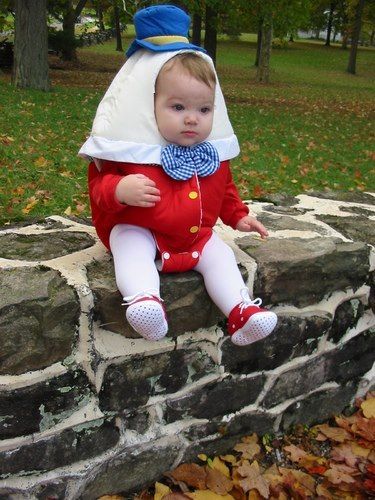 a baby sitting on top of a stone wall wearing a red and white outfit with a blue bow tie