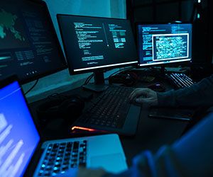 a man sitting in front of three computer monitors with laptops on the desk next to him