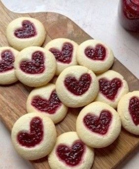 heart shaped cookies on a cutting board with jam in the middle and two jars of jelly behind them