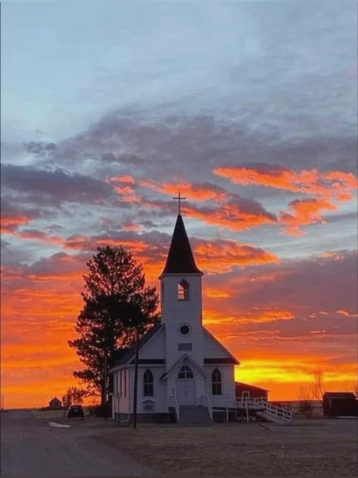 a church with a steeple at sunset in the background and trees on the other side