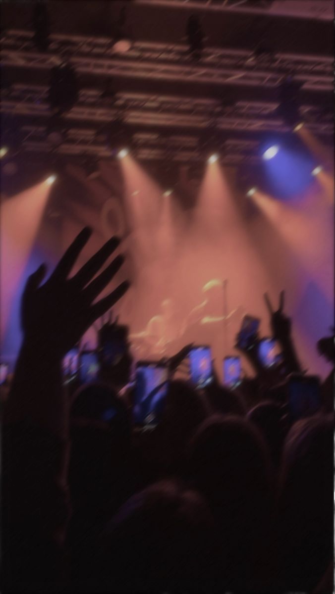 a crowd of people at a concert with their hands in the air and lights on