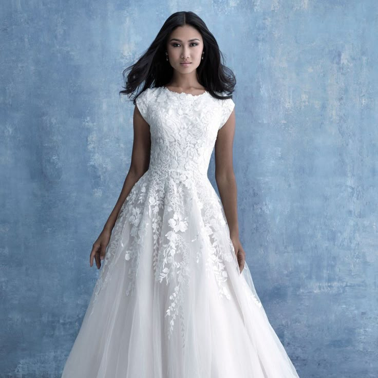 a woman in a white wedding dress standing against a blue wall with her hands on her hips