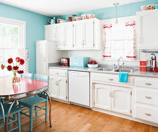 a kitchen with blue walls and white cabinets, wood flooring and a table in the middle