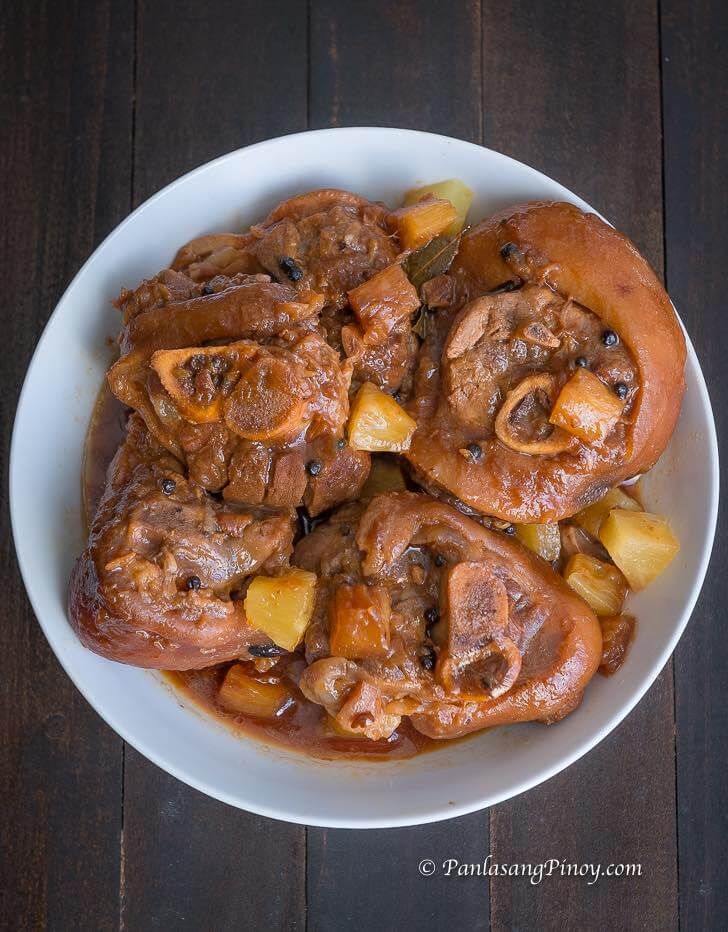 a bowl filled with meat and potatoes on top of a wooden table next to a fork