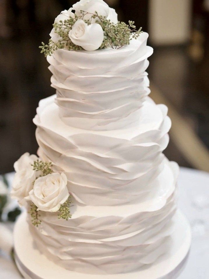 a three tiered white wedding cake with flowers on top