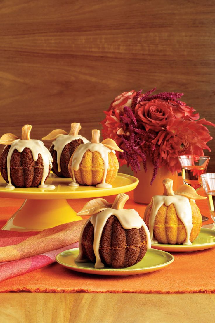 a table topped with cakes covered in frosting and pumpkins next to a vase filled with flowers