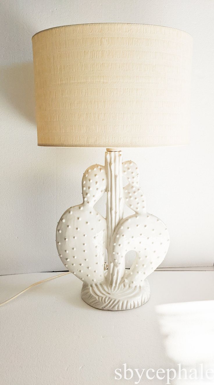 a white lamp sitting on top of a table next to a lampshade and a wall