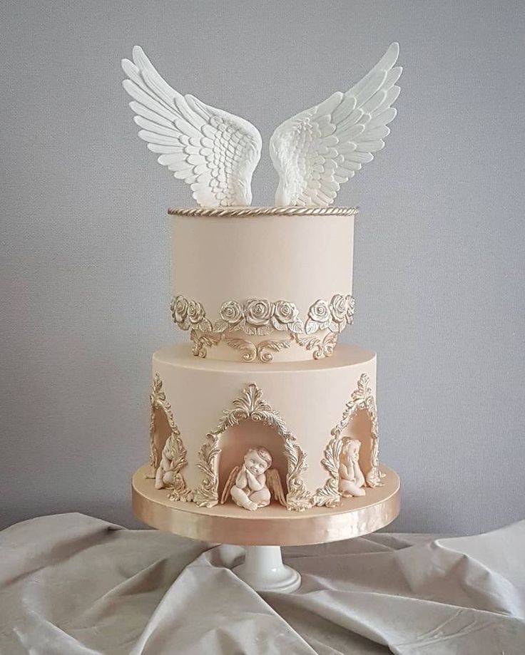 a three tiered cake with angel wings on top is sitting on a white tablecloth