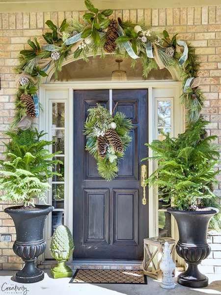 a front door decorated with potted plants and greenery for the holiday season,