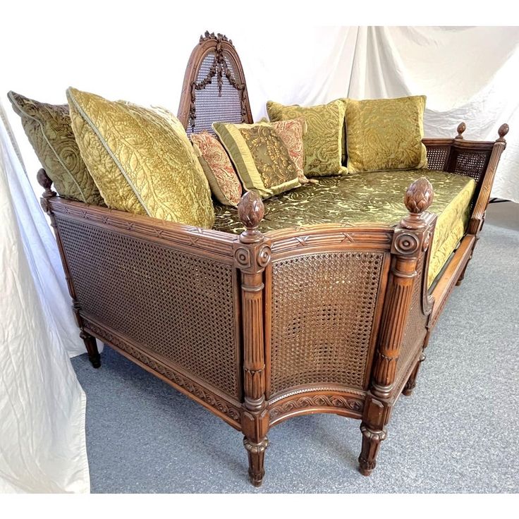 a wicker bed with green cushions and pillows on it's headrests