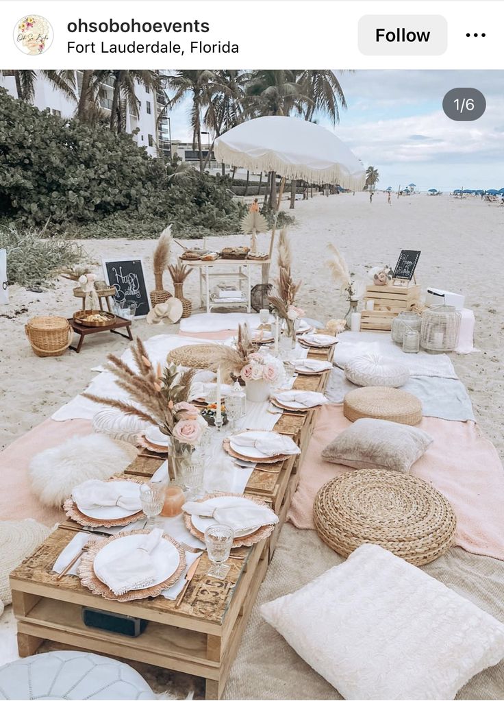 a table set up on the beach with plates and place settings in front of it