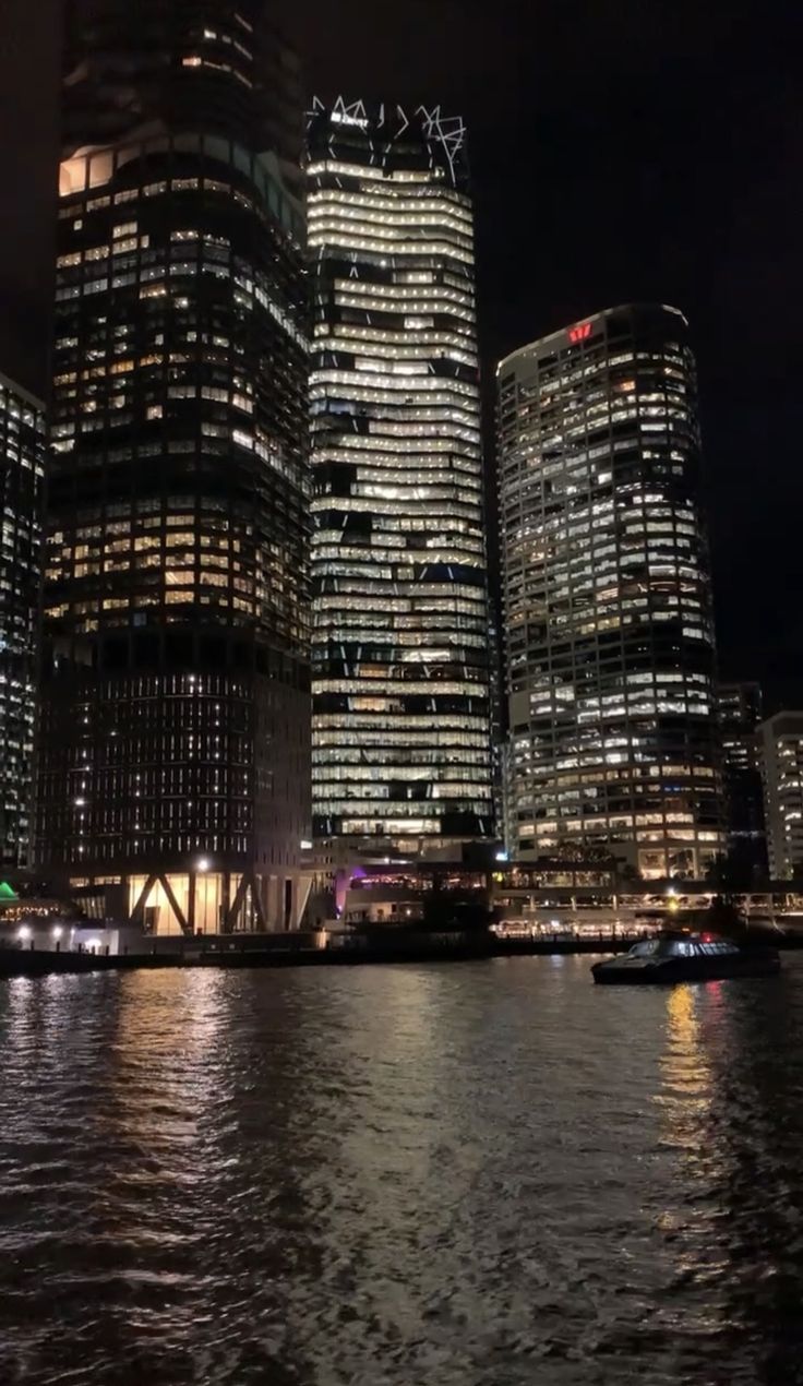 some very tall buildings by the water at night