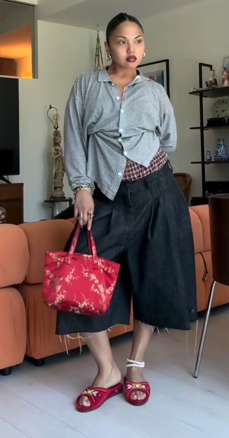 a woman holding a red purse standing in front of a couch