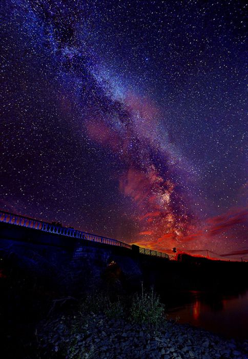 the night sky is filled with stars and bright lights, as seen over a river