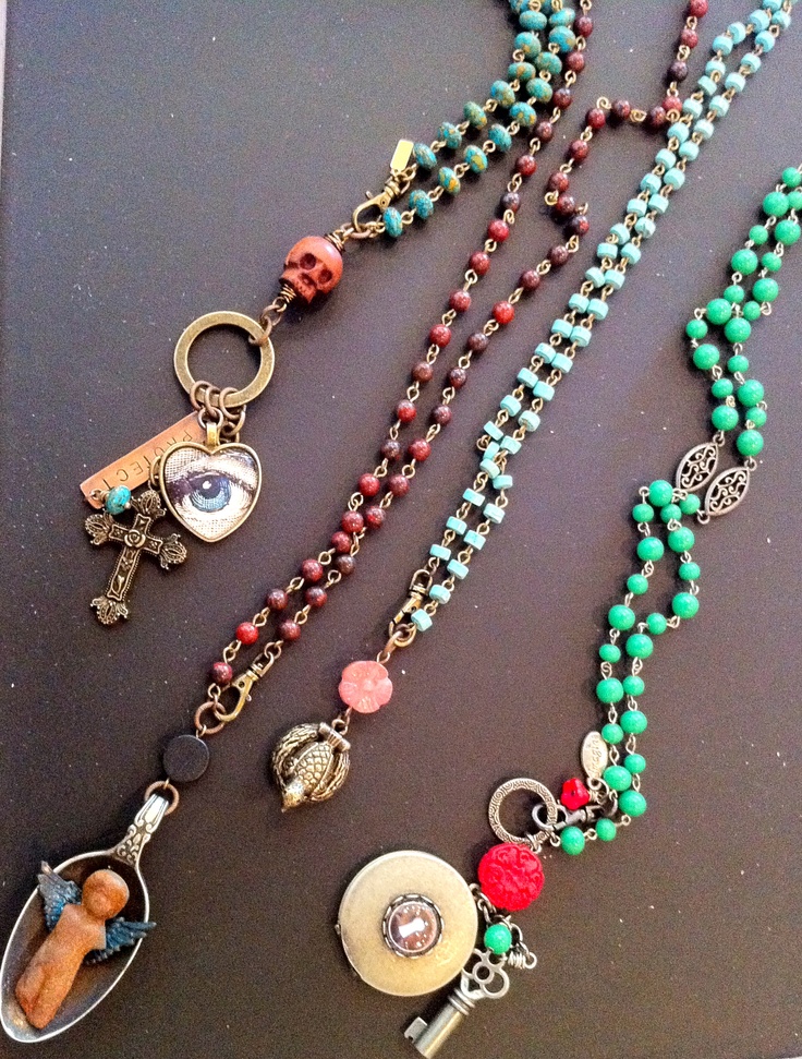 several necklaces with beads and charms on a black surface next to an orange cell phone