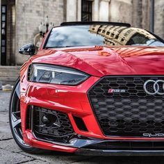 the front end of a red sports car parked in front of a brick building on a city street