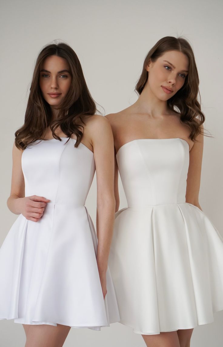 two women in white dresses standing next to each other, one wearing a short dress