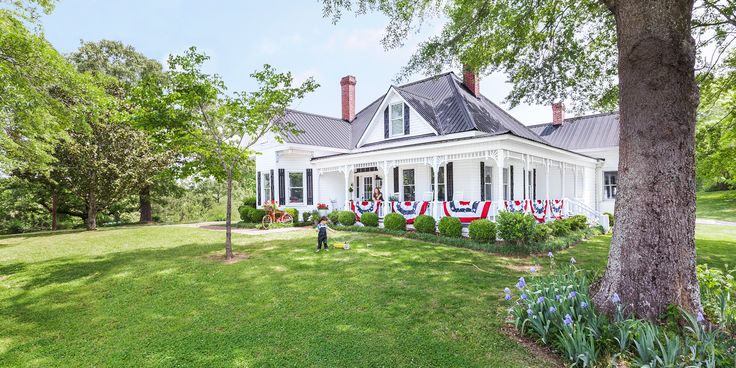 a white house with an american flag on the front lawn and trees in the back yard