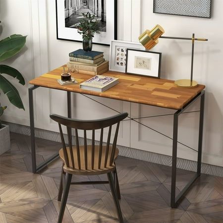 a wooden desk topped with books next to a chair and framed pictures on the wall