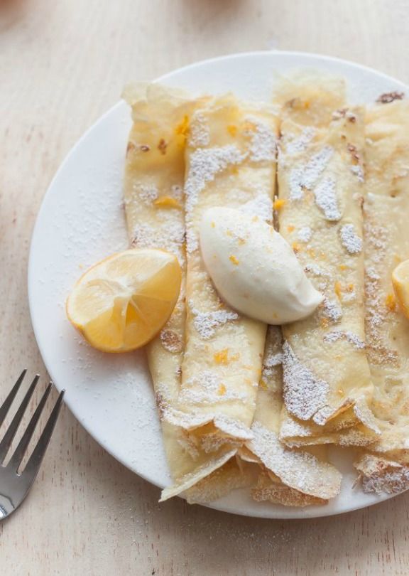 a white plate topped with crepes covered in powdered sugar and lemon wedges