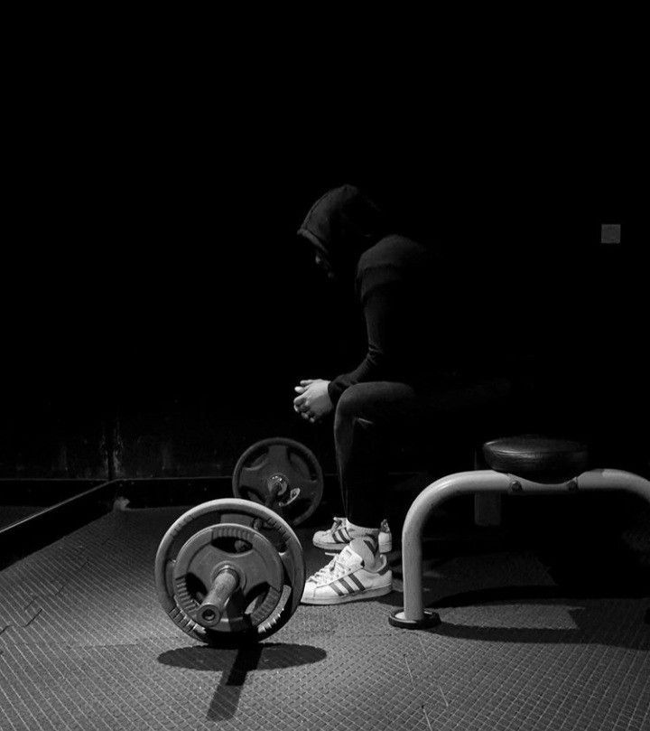 a person squatting in the dark with their feet on a barbell and another bench behind them