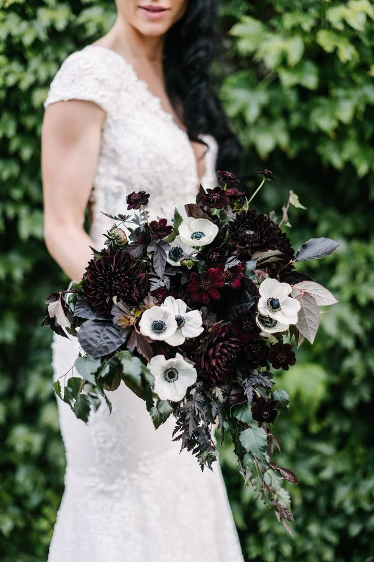 a woman holding a bouquet of flowers on her wedding day in front of greenery