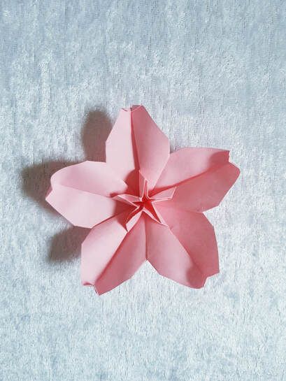 a pink origami flower sitting on top of a white tablecloth covered floor