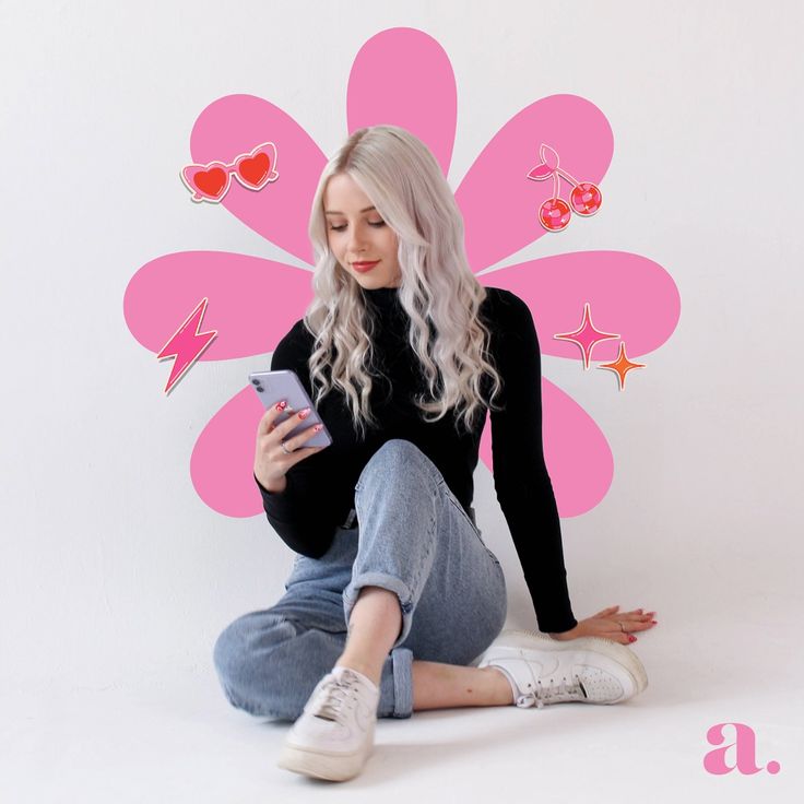 a woman sitting on the floor with her cell phone in front of a pink flower