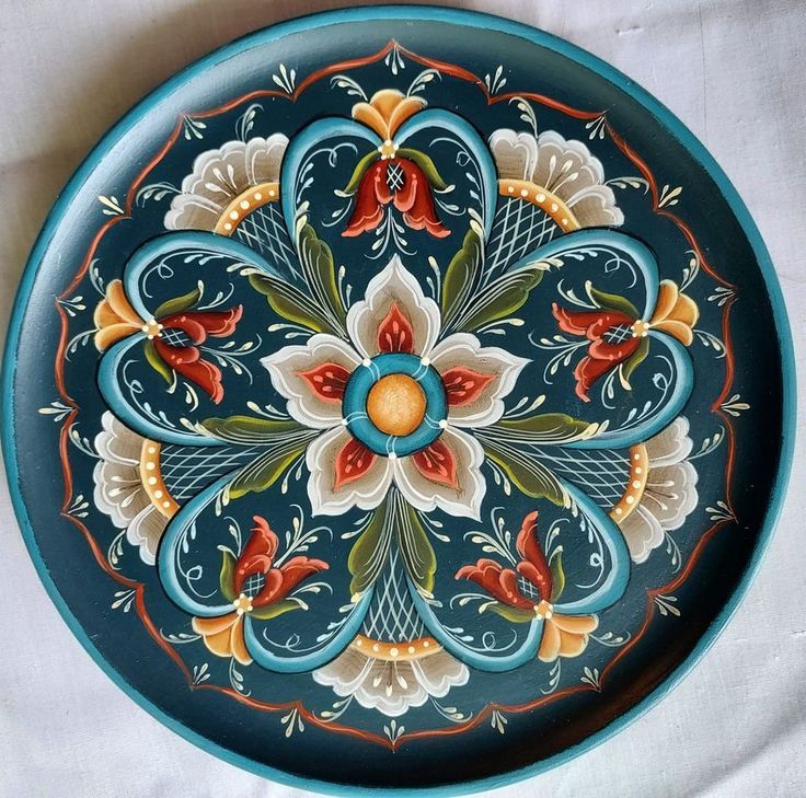 a decorative blue plate with red and yellow flowers painted on the side, sitting on a white cloth