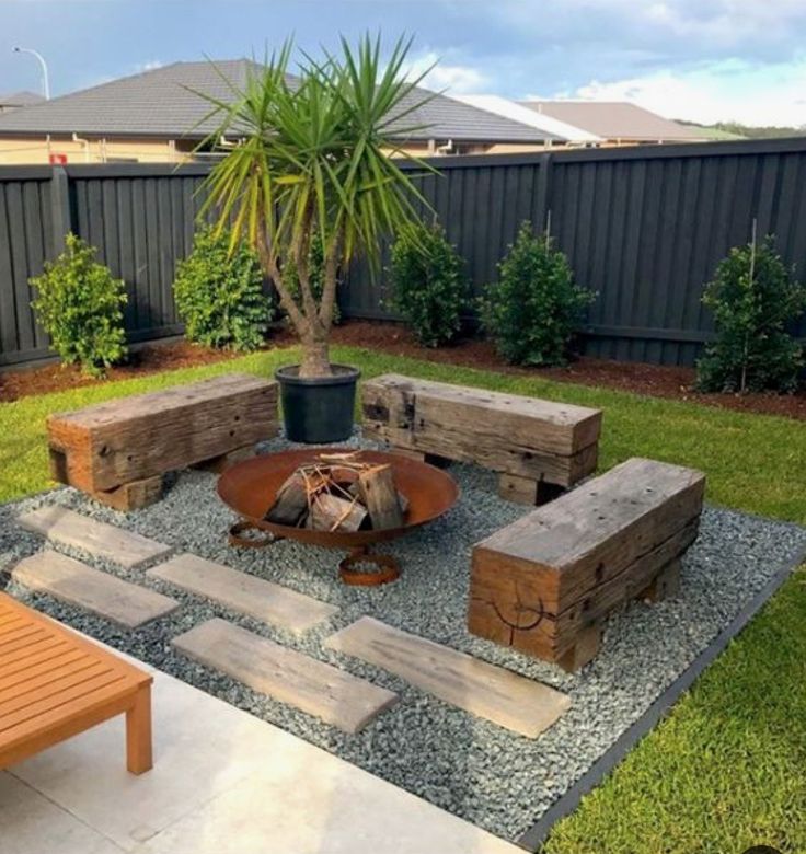 an outdoor fire pit in the middle of a yard with benches and a potted plant