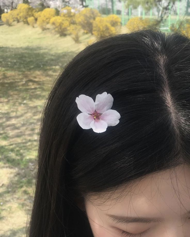 a close up of a person with a flower in their hair and grass behind her