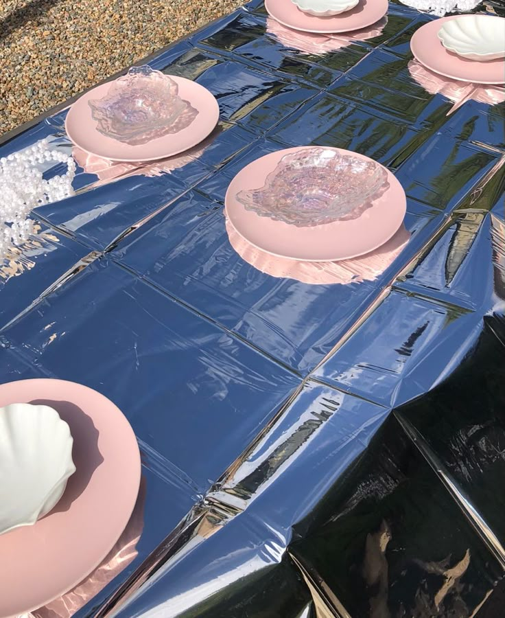 pink and white plates sitting on top of a table covered in blue tarp next to shells