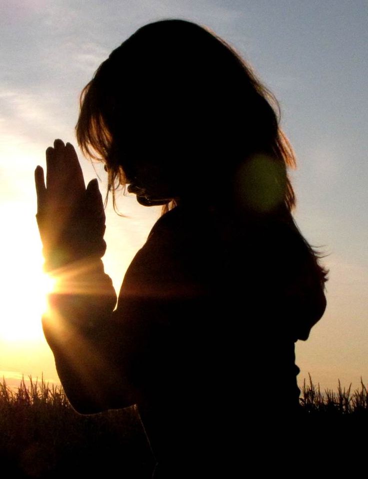 the silhouette of a woman praying in front of the sun with her hands clasped up