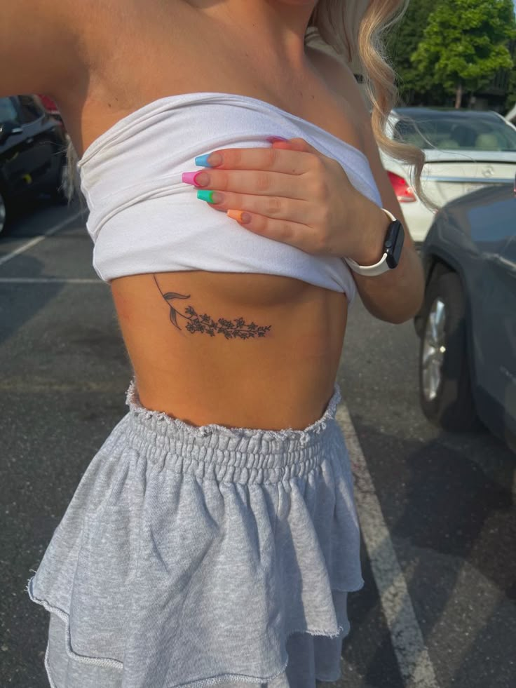 a woman with a tattoo on her stomach standing in a parking lot next to a car