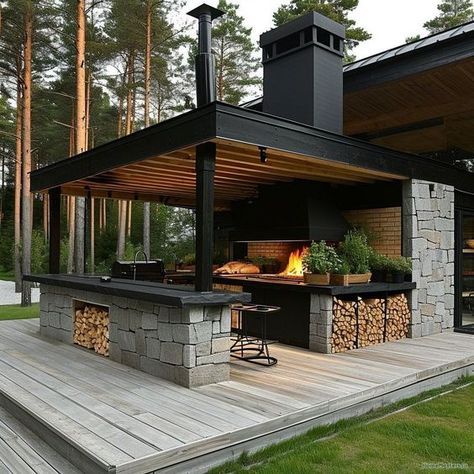 an outdoor kitchen on a deck in the middle of a forest with firewood stacked under it