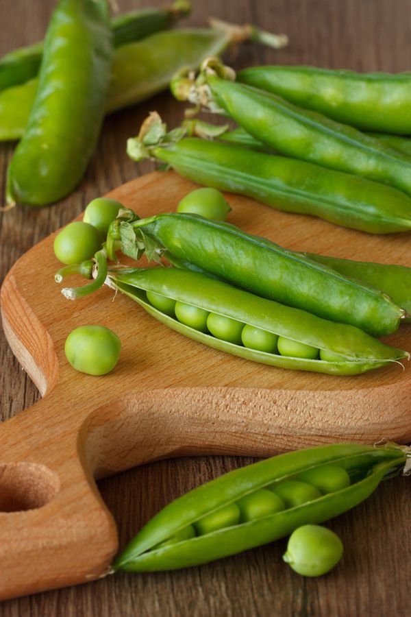 peas and pea pods on a wooden cutting board