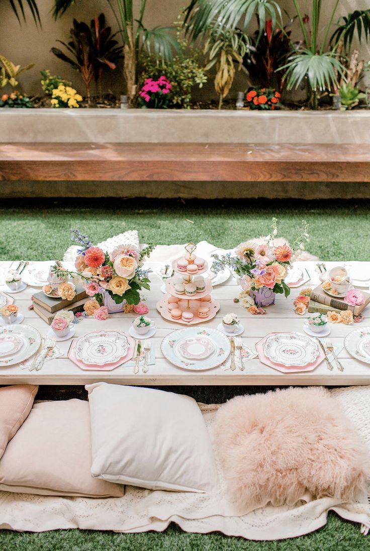 a table set up with pink and white plates, flowers and desserts on it