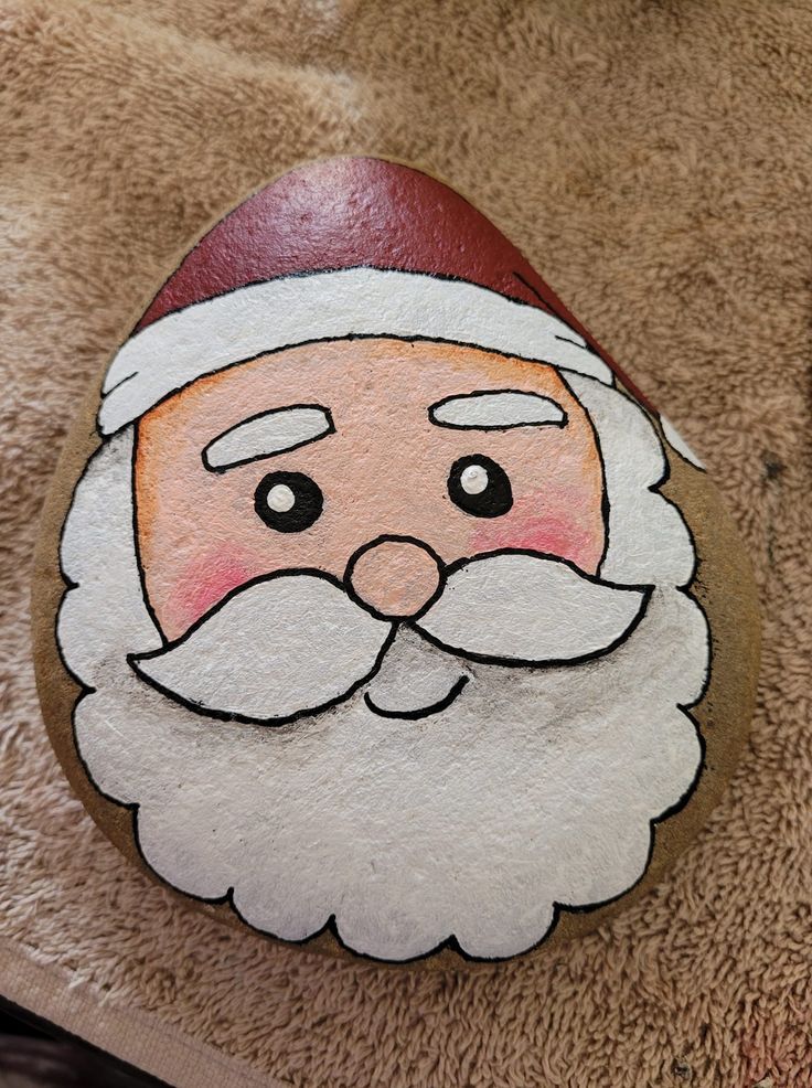 a painted rock with a santa claus face on it's side, sitting on the ground