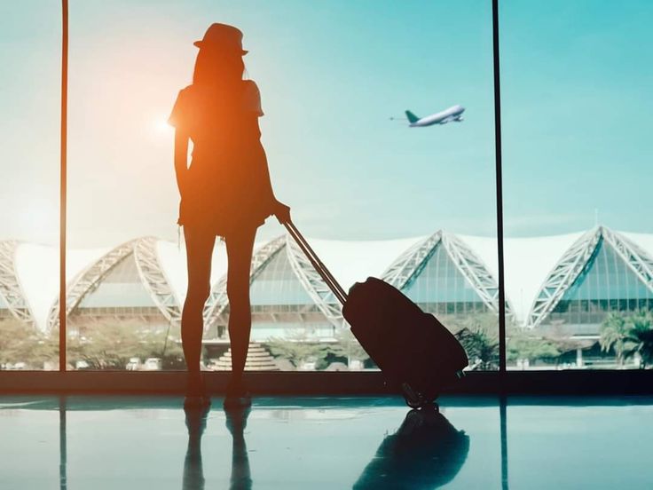 a woman is standing in an airport with her luggage and looking out the window at planes